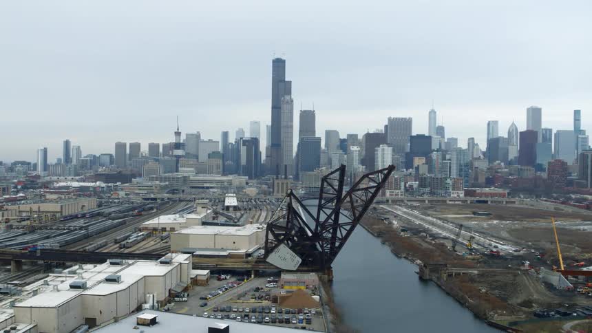 An aerial view of an industrial train yard and factories with the chicago skyline in the background on an overcast day