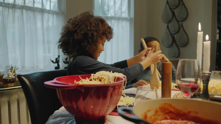 Girl serving a messy spoonful of pasta to her brother in the dinning table at home