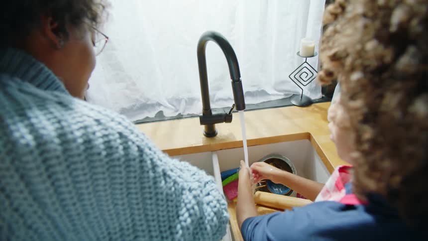 Mother and daughter stand at kitchen sink washing their hands
