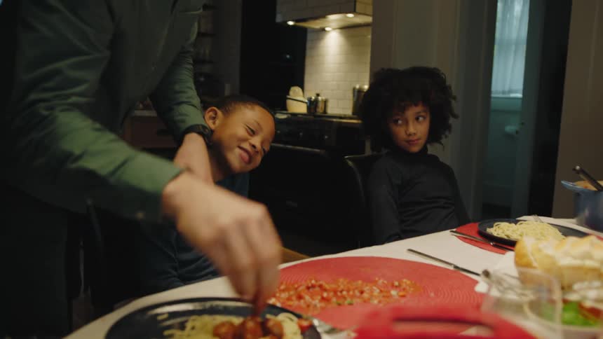 A dad tries to calm his son down and cleans up the mess he made at the dinner table