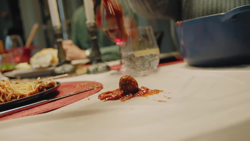 Spaghetti and meatballs are being poured on the dining room table