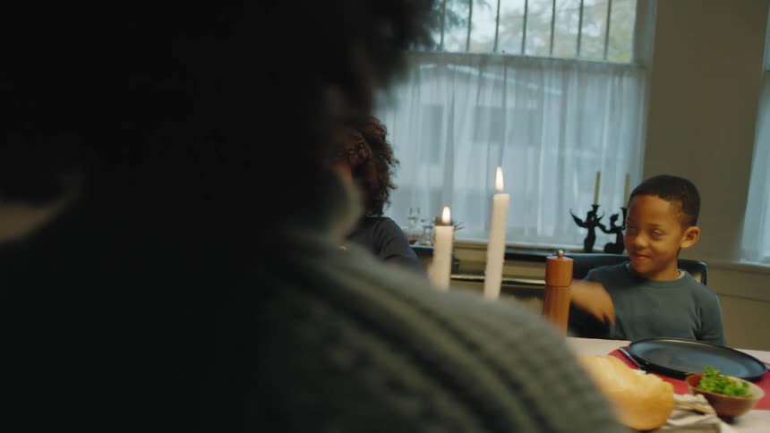 Family of four sit at the dinner table while the daughter serves spaghetti