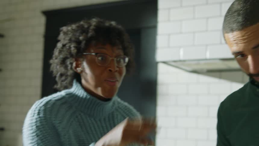 Mother gestures while talking as family works around counter in kitchen