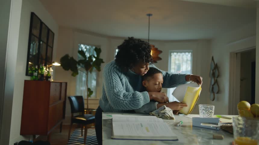 Mother helps son to dry spilled orange juice from a notebook in the living room