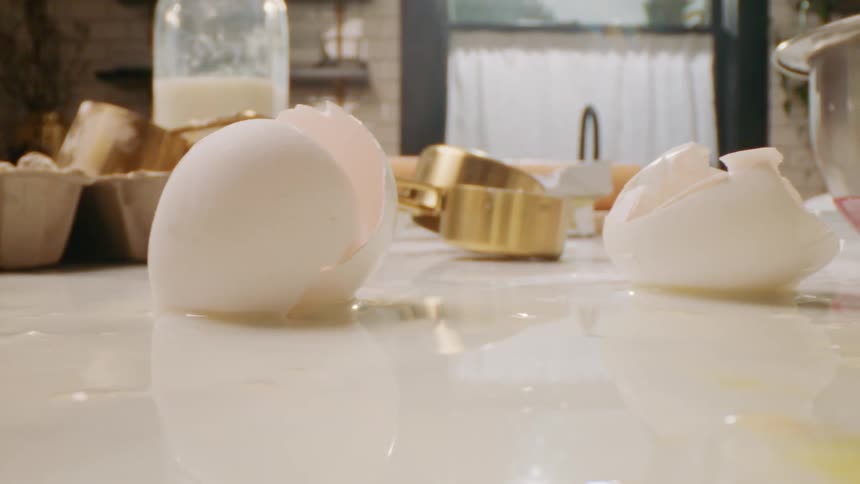 Mess of chocolate chips and egg shells sits on marble counter near mixing bowls