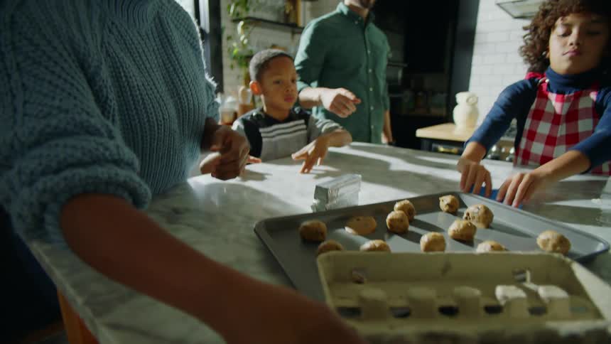 Family cleans kitchen island and puts left over ingredients away while cookie dough sits on cookie sheet