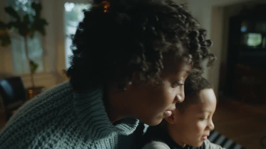 A woman helps her son to draw with markers in a notebook at a kitchen counter