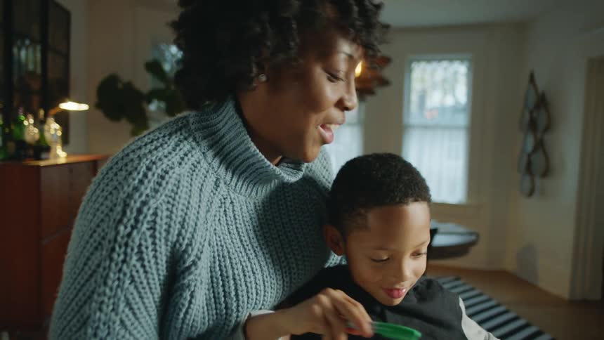 Mother kisses son while helping with homework on the living room at home