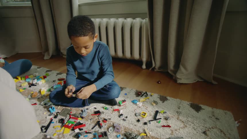 A child is sitting on a rug at home and playing with a collection of lego blocks during the day