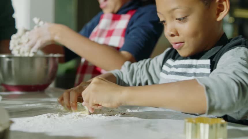 Brother and sister kneading and cutting cookies in the kitchen at home