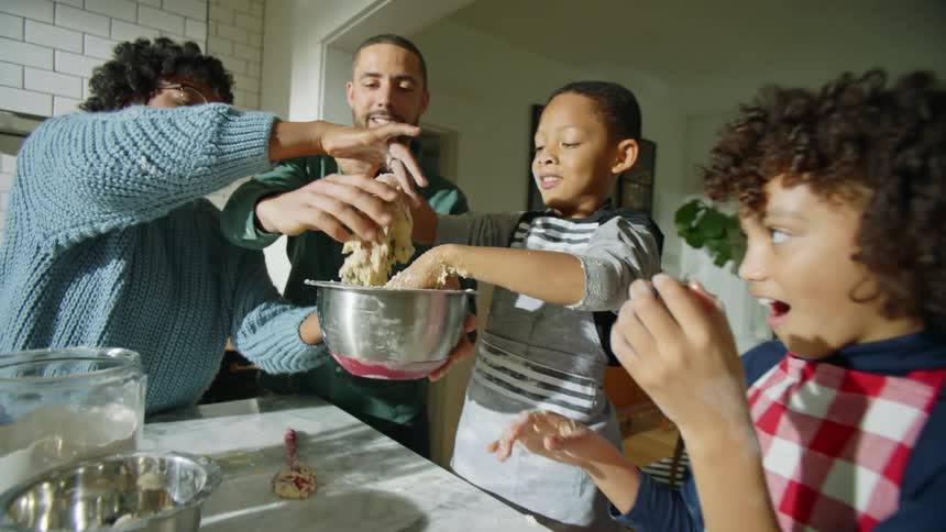 Mother and father help son knead dough as sister gapes