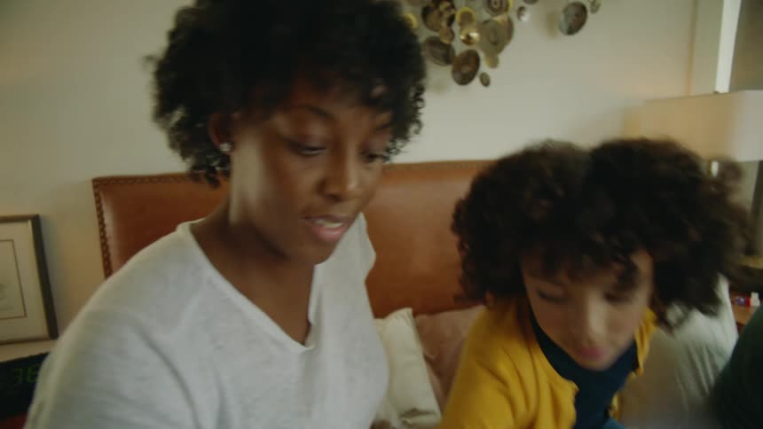 A man and woman sit on a bed with their daughter and they all put toys in a bin