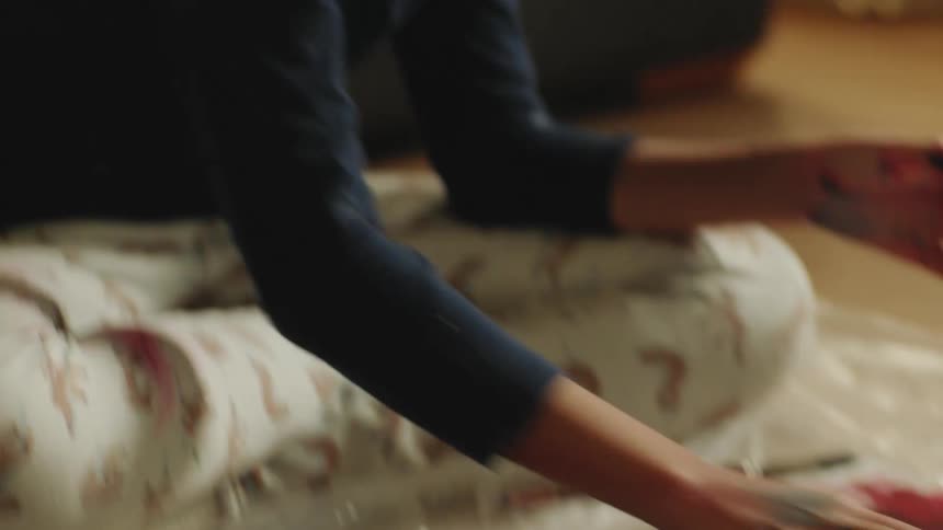 A girl sits on the floor in her living room and smears paint on a canvas with her fingers