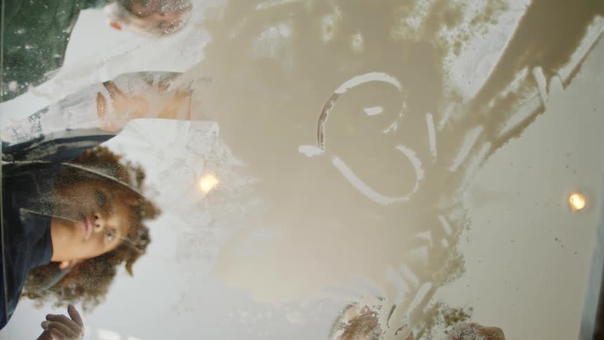 Daughter draws in flour on glass surface as others watch