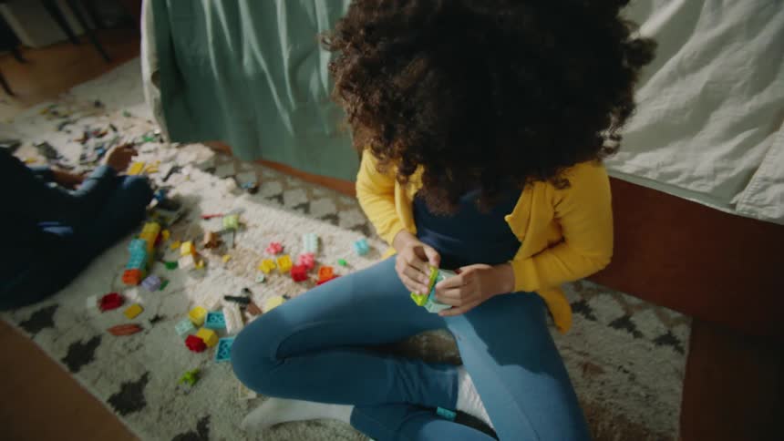A girl and boy play with legos while sitting on the floor of a bedroom