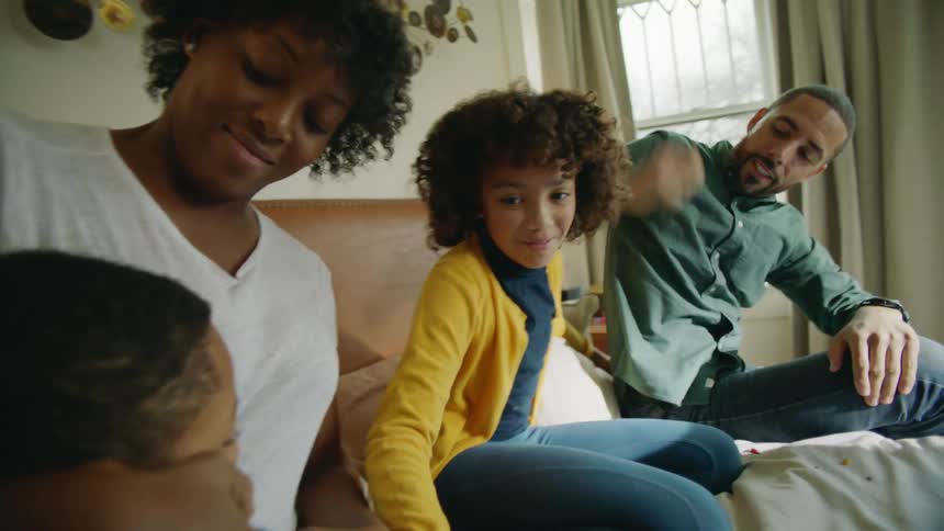 Family of four playing over the bed in the bedroom at home