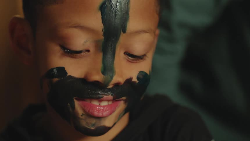 Young boy with his face covered in paint talks to his parents