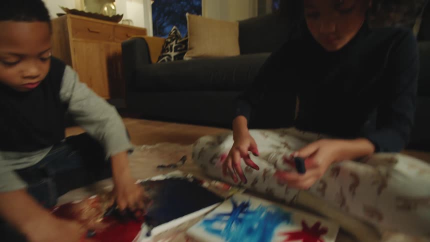Brother and sister sitting on the living room floor painting with brushes and fingers