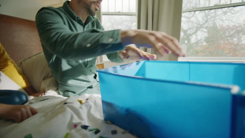 Parents help daughter to pick up toys over the bed at home