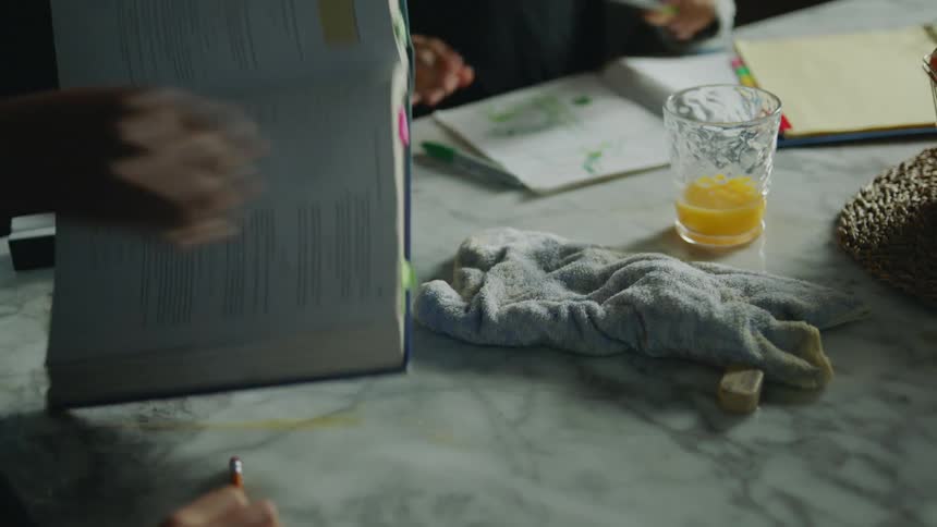 A woman uses a washcloth to clean up spilled orange juice from a kitchen counter and textbook