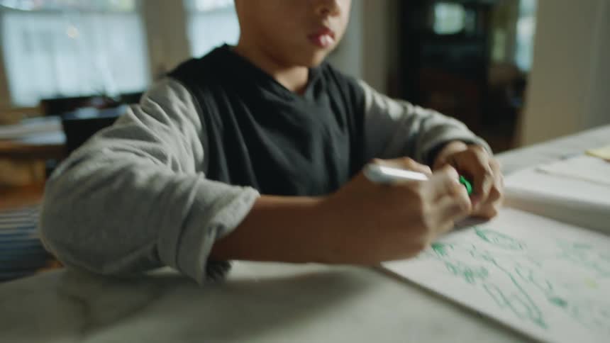 A young boy is sitting at a table drawing a picture with a green marker