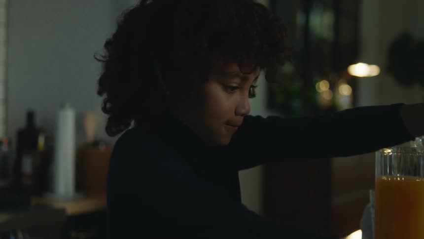 A girl reaches for a washcloth to clean spilled orange juice off her homework as her parents approach to help