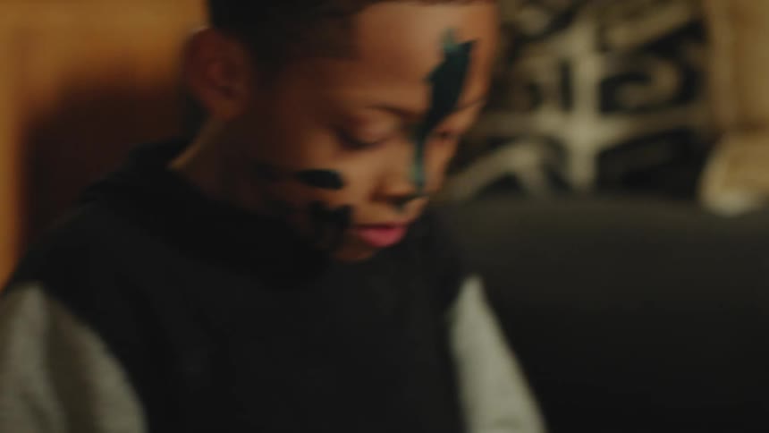 Boy with paint on his face makes faces and takes a pose playing in living room