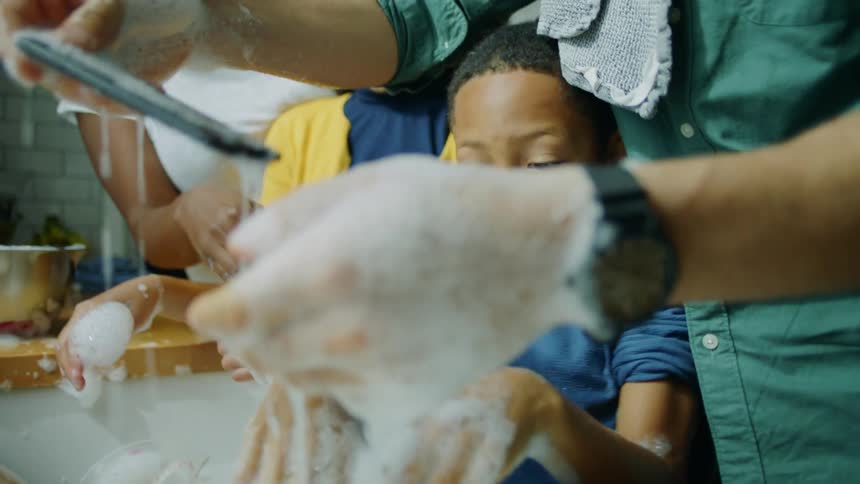 Boy washing dishes at home slaps the phone from his father hand throwing it into the sink