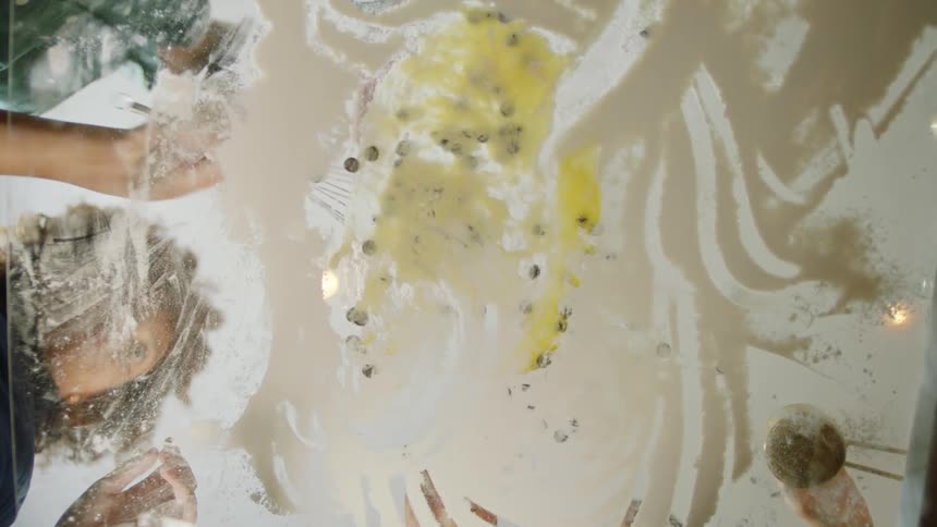 People stir food mixture on glass surface
