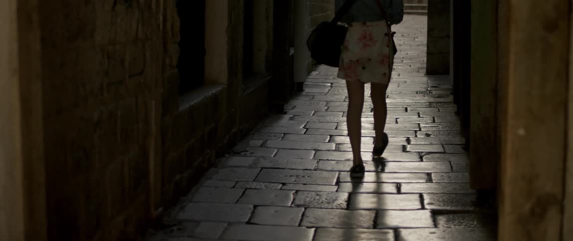 A woman walks down a brick alley between two buildings