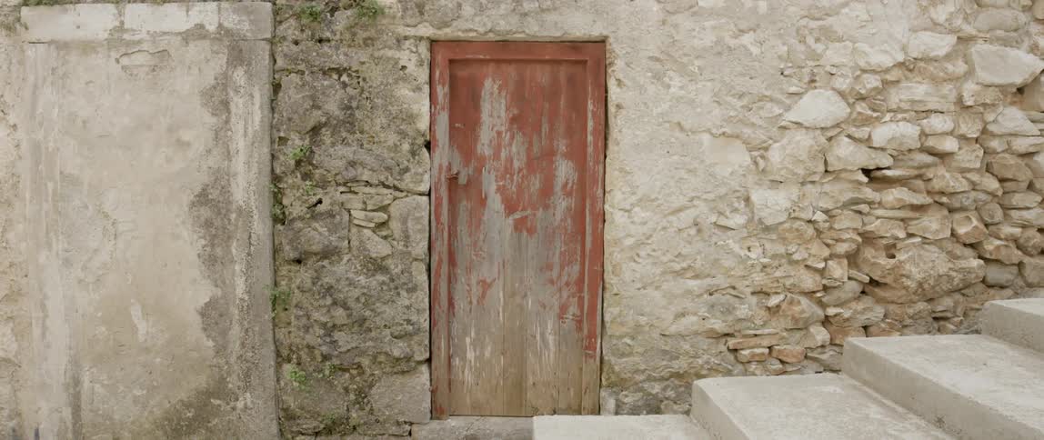 A small red door is on the side of a stone wall
