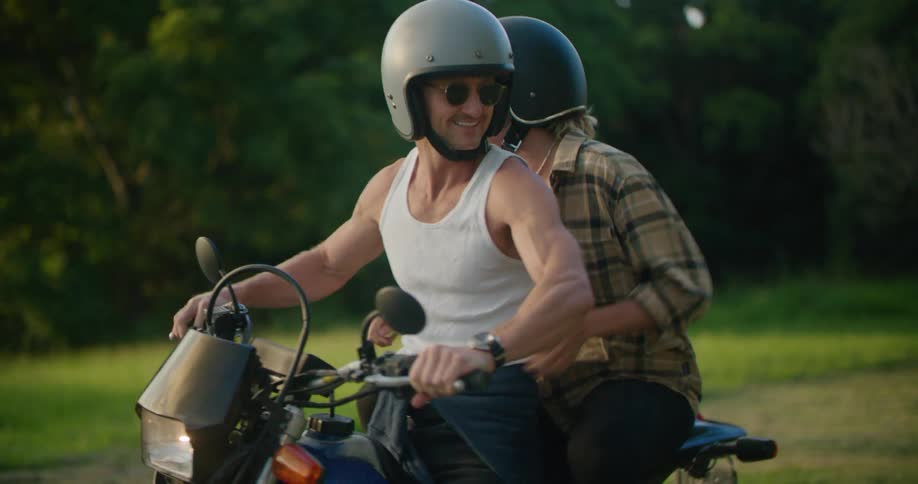 A woman gets on the back of a motorcycle and holds on tight as her man drives away