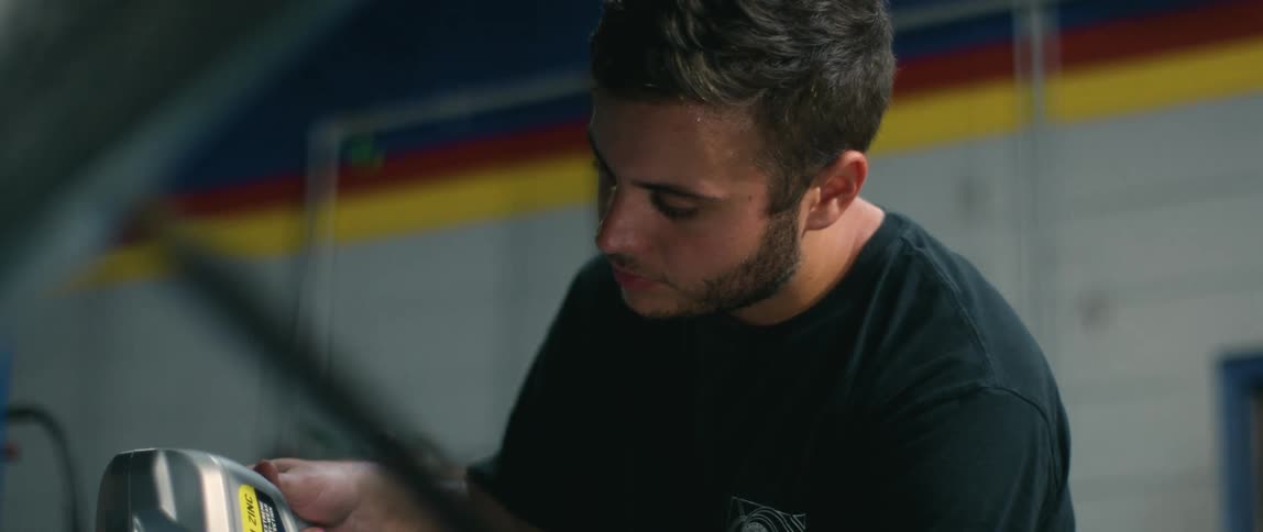 Young mechanic pouring oil in the engine of a car inside an auto repair shop
