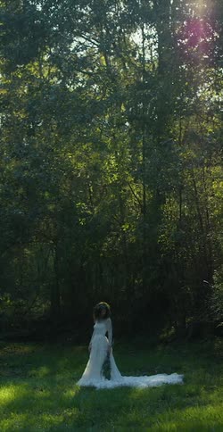Bride with wedding dress stands in front of trees in the woods