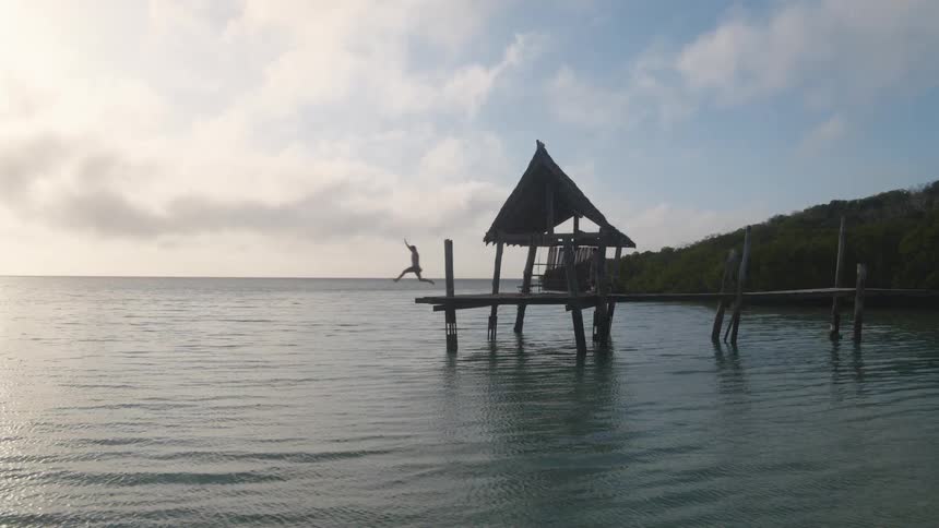 Man jumps off wooden pier at sunset