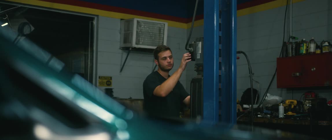 An auto technician activates a hydraulic lift to raise a car in a repair shop during the daytime