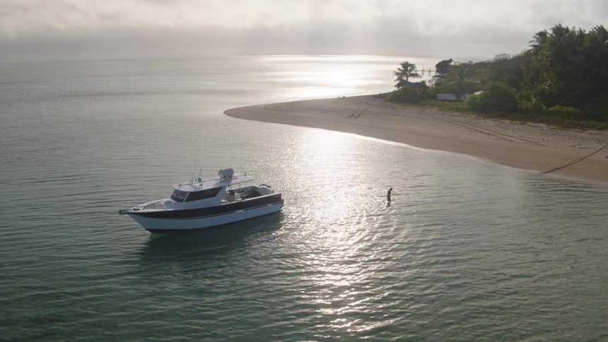 A man stands in the water by the moving ship