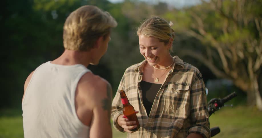 Young couple sitting on a parked motorcycle drinking beer at sunset