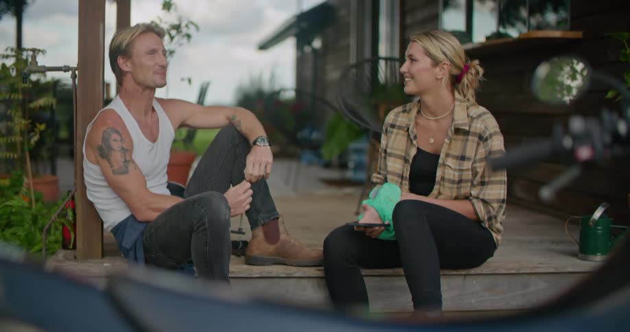 A man and woman chat while sitting together on the porch of a house on a cloudy day
