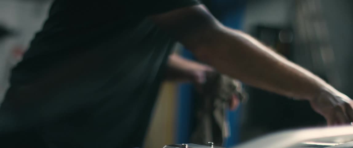 A man removes a funnel from the engine of a vehicle in a garage during the day