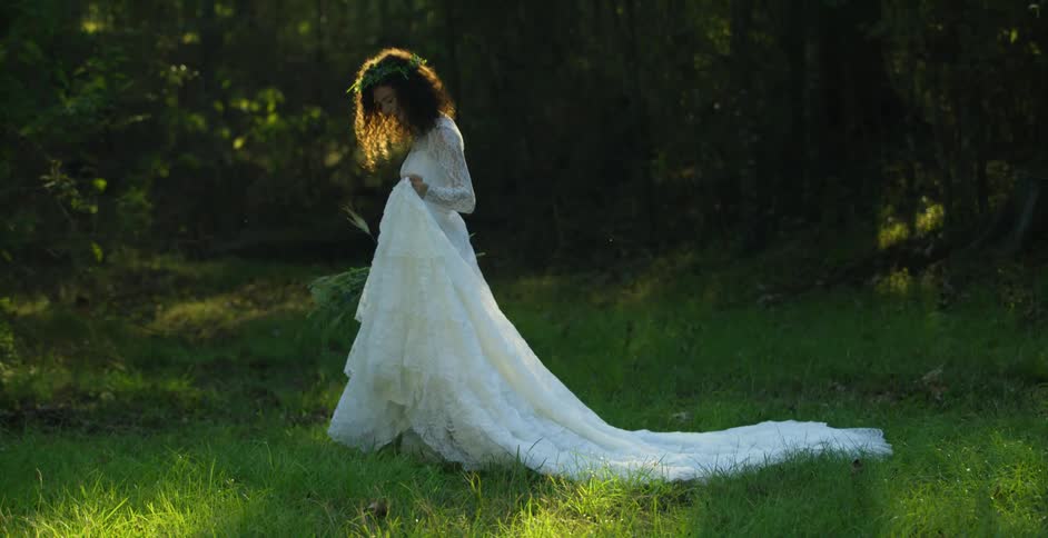 A bride dressed in her wedding dress is walking in a clearing in a woodland area during the day