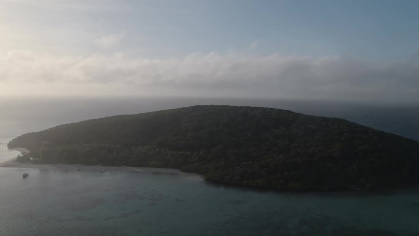 Waves roll over the shore of an island under a hazy cloudy sky