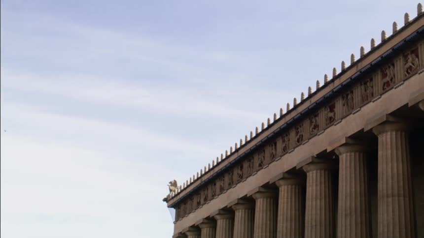 Flock of birds fly over building decorated with columns and carved stone
