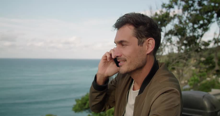 Young man standing on the road talks on the phone near the ocean at sunset