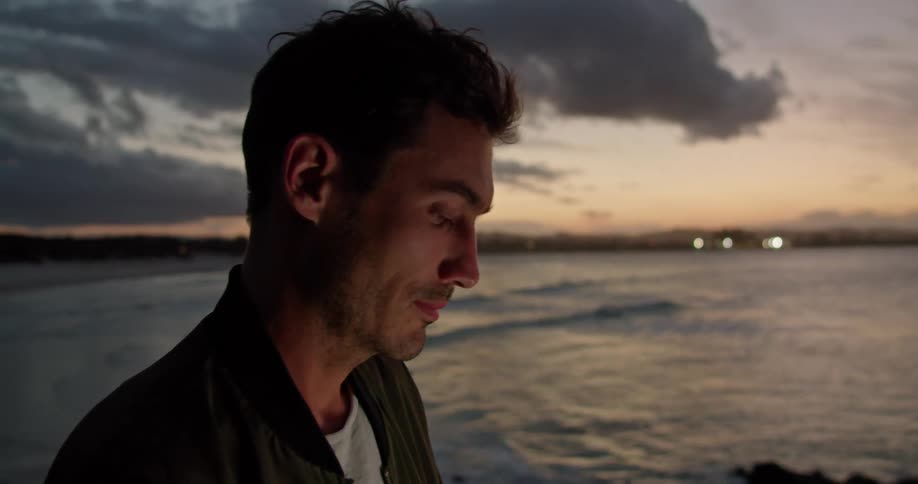 Young man working on a laptop over a handrail near the beach at sunset