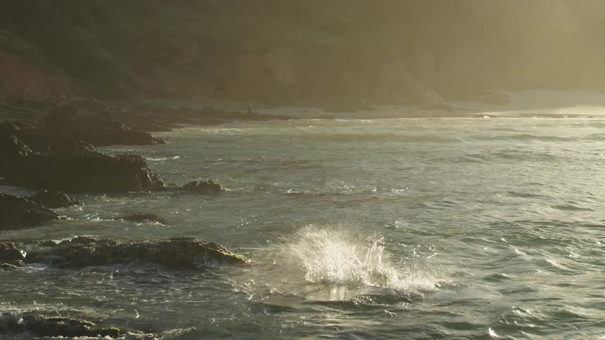 A man is standing on rocks along the coast and dives into the water as the sun is shining brightly