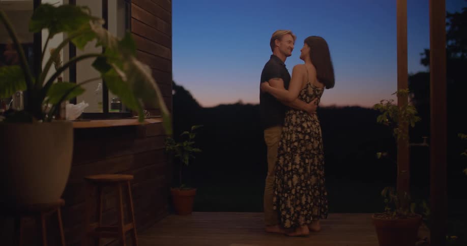 Couple slow dances barefoot on wooden porch at night