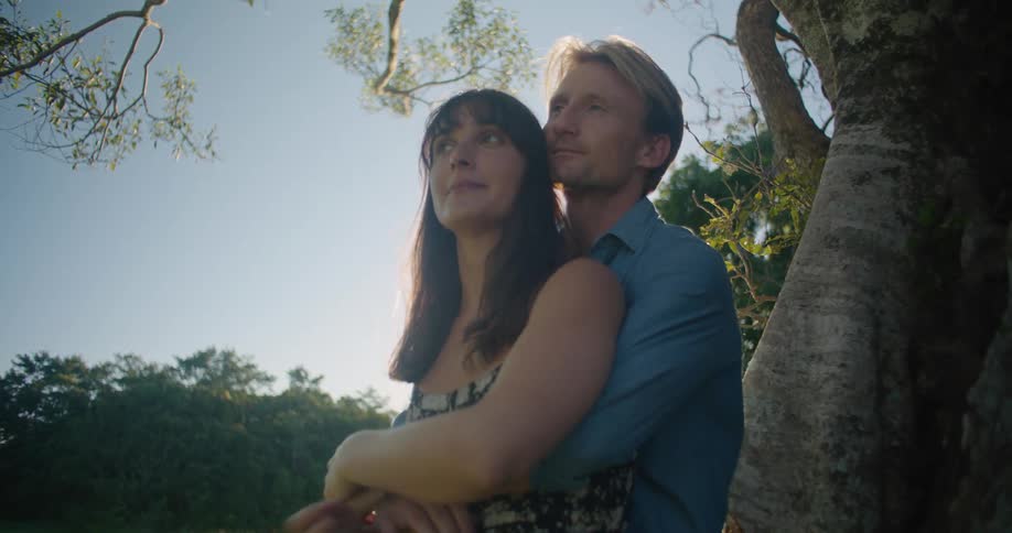 A man is leaning against a tree with his arms around a woman