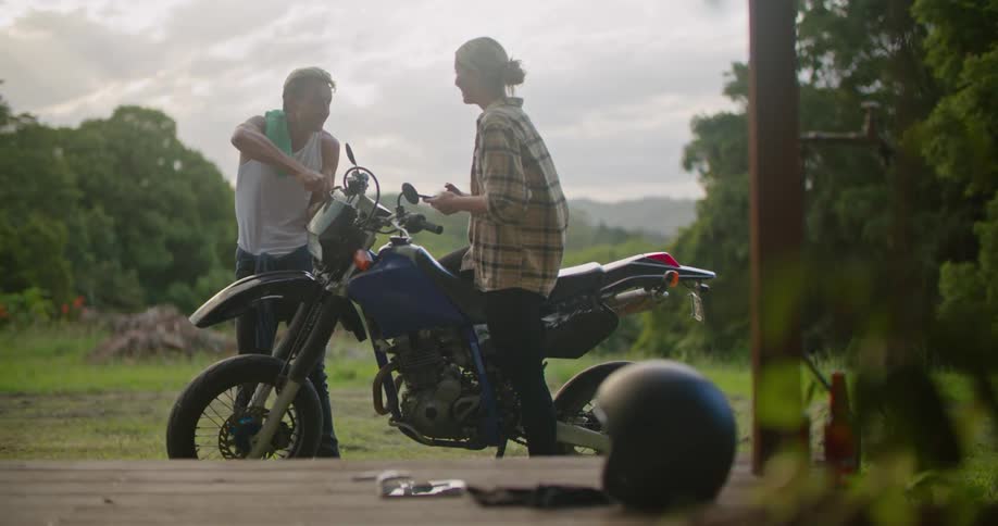 A man fixes a motorcycle while a woman talks to him
