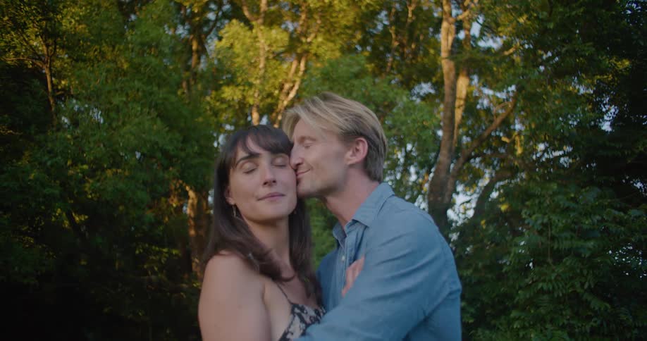 Young couple hug and kiss caringly in front of trees at evening